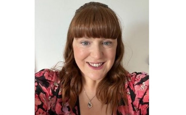 Laura Lindsay smiling, wearing a top with large pink flowers and a heart necklace