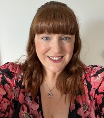 Laura Lindsay smiling, wearing a top with large pink flowers and a heart necklace