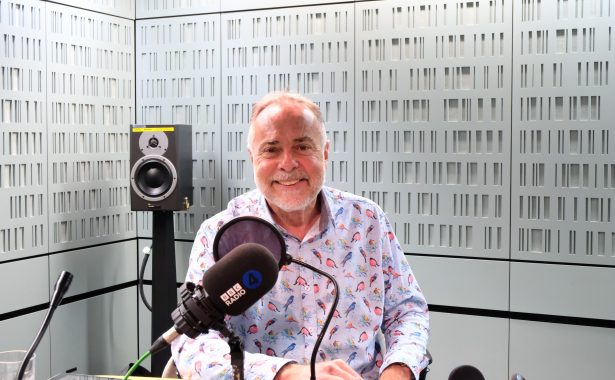 Gerard sits in a BBC radio recording studio wearing a colourful shirt and smiling for the camera.