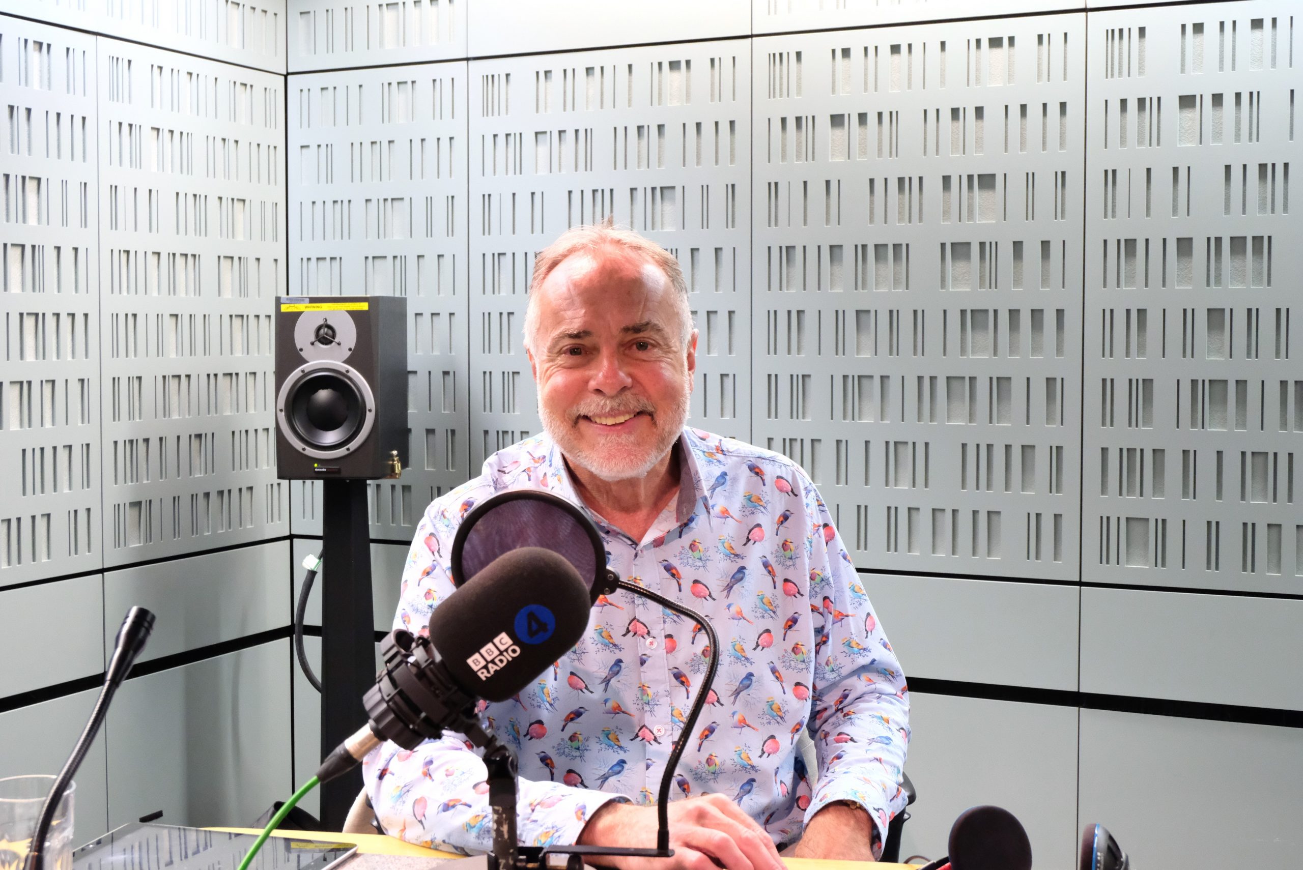 Gerard sits in a BBC radio recording studio wearing a colourful shirt and smiling for the camera.