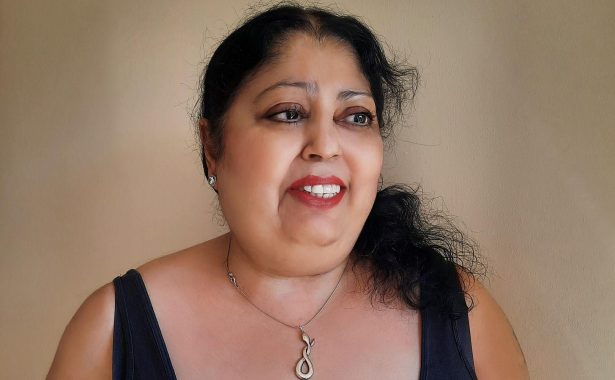 Kim Jaye smiling with her long, black hair tied back. She is wearing a black vest, stud earrings and a necklace with a snake pendant.