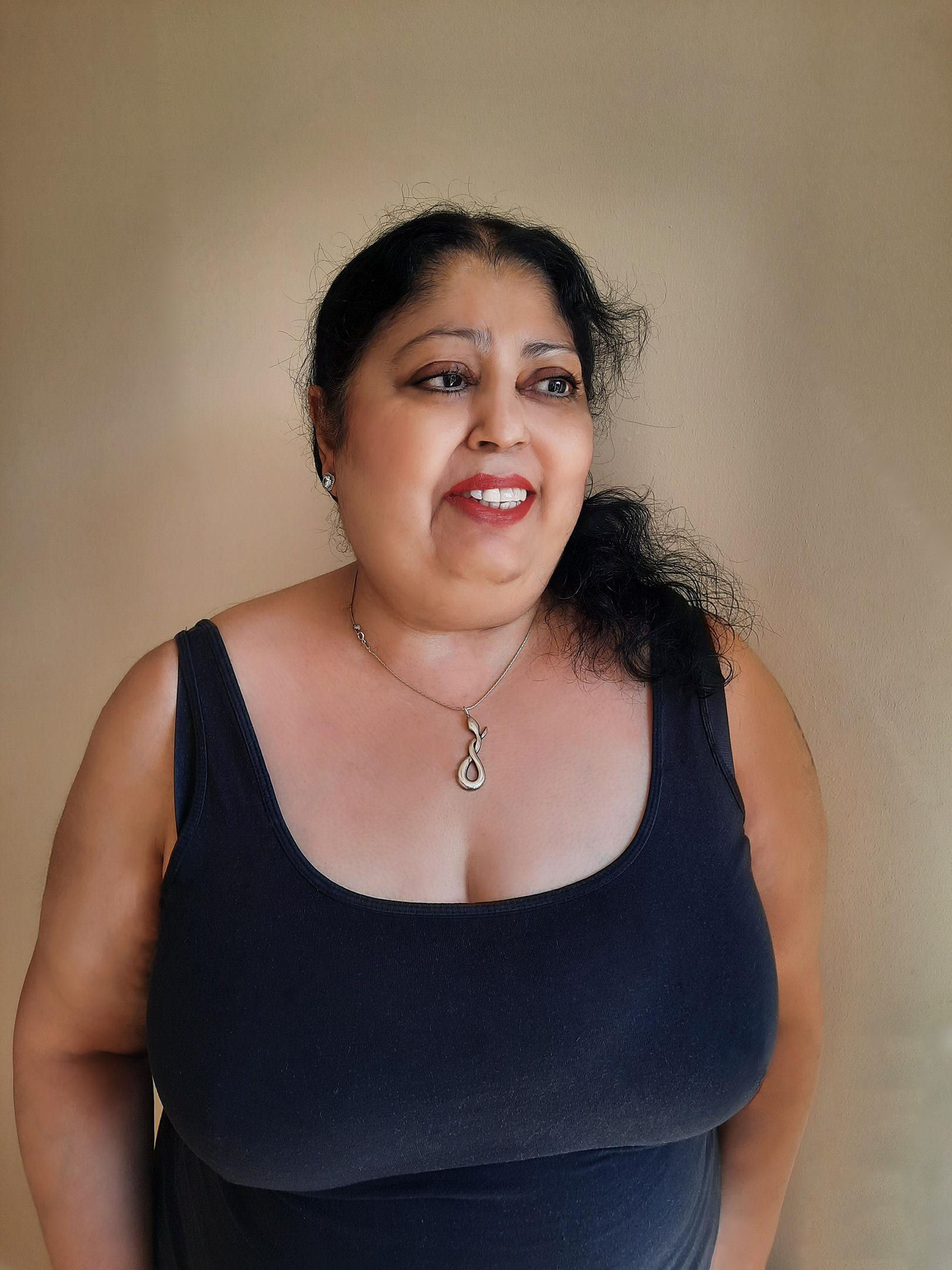 Kim Jaye smiling with her long, black hair tied back. She is wearing a black vest, stud earrings and a necklace with a snake pendant. 