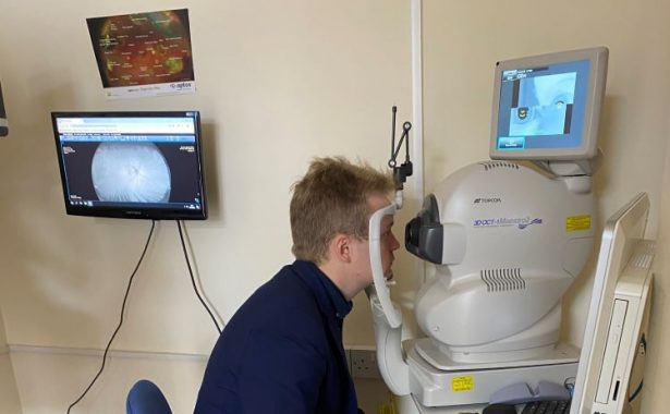 Euan Stainbank MP sitting wearing a navy blue, sitting in a chair taking an eye test. Image of the back of his eye is on a screen behind him.