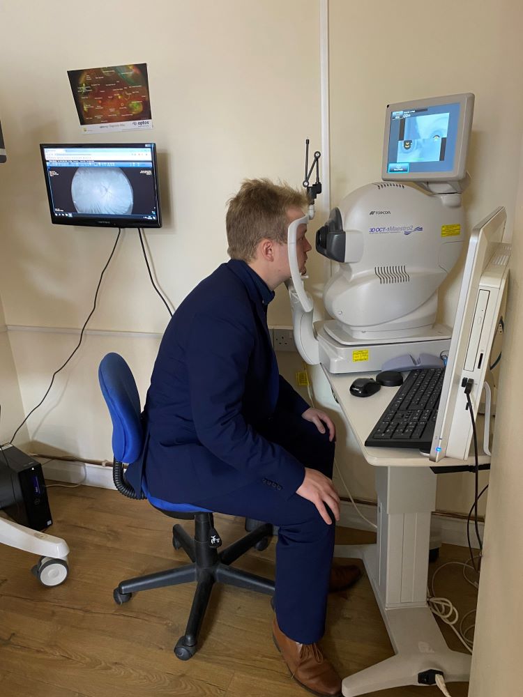 Euan Stainbank MP sitting wearing a navy blue, sitting in a chair taking an eye test. Image of the back of Euan's eye is on a screen behind him.