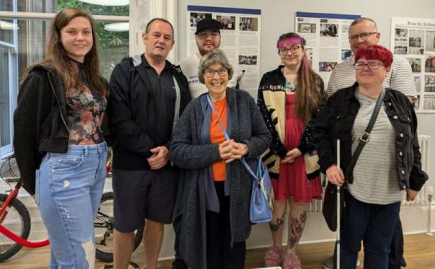 A group of volunteers smiling, with an exhibition behind them.