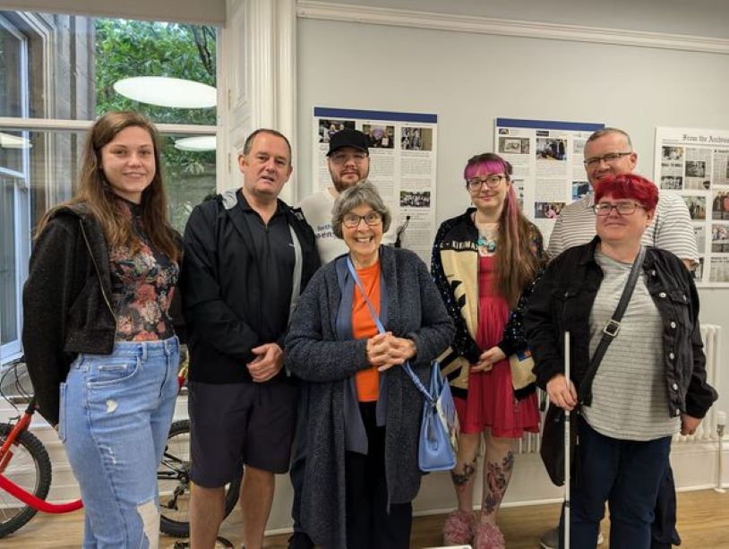 A group of volunteers smiling, with an exhibition behind them.