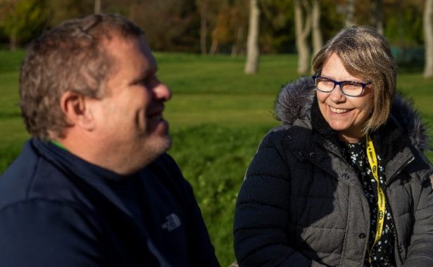 A vision impaired person and a member of the Vision Support Barrow & District team sat smiling at one another in Barrow Park. Photo courtesy of Vision Support Barrow & District.