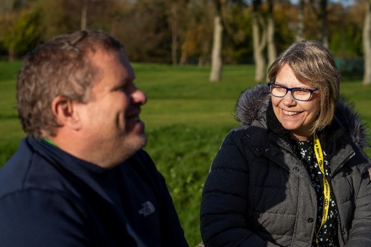 A vision impaired person and a member of the Vision Support Barrow & District team sat smiling at one another in Barrow Park. Photo courtesy of Vision Support Barrow & District.