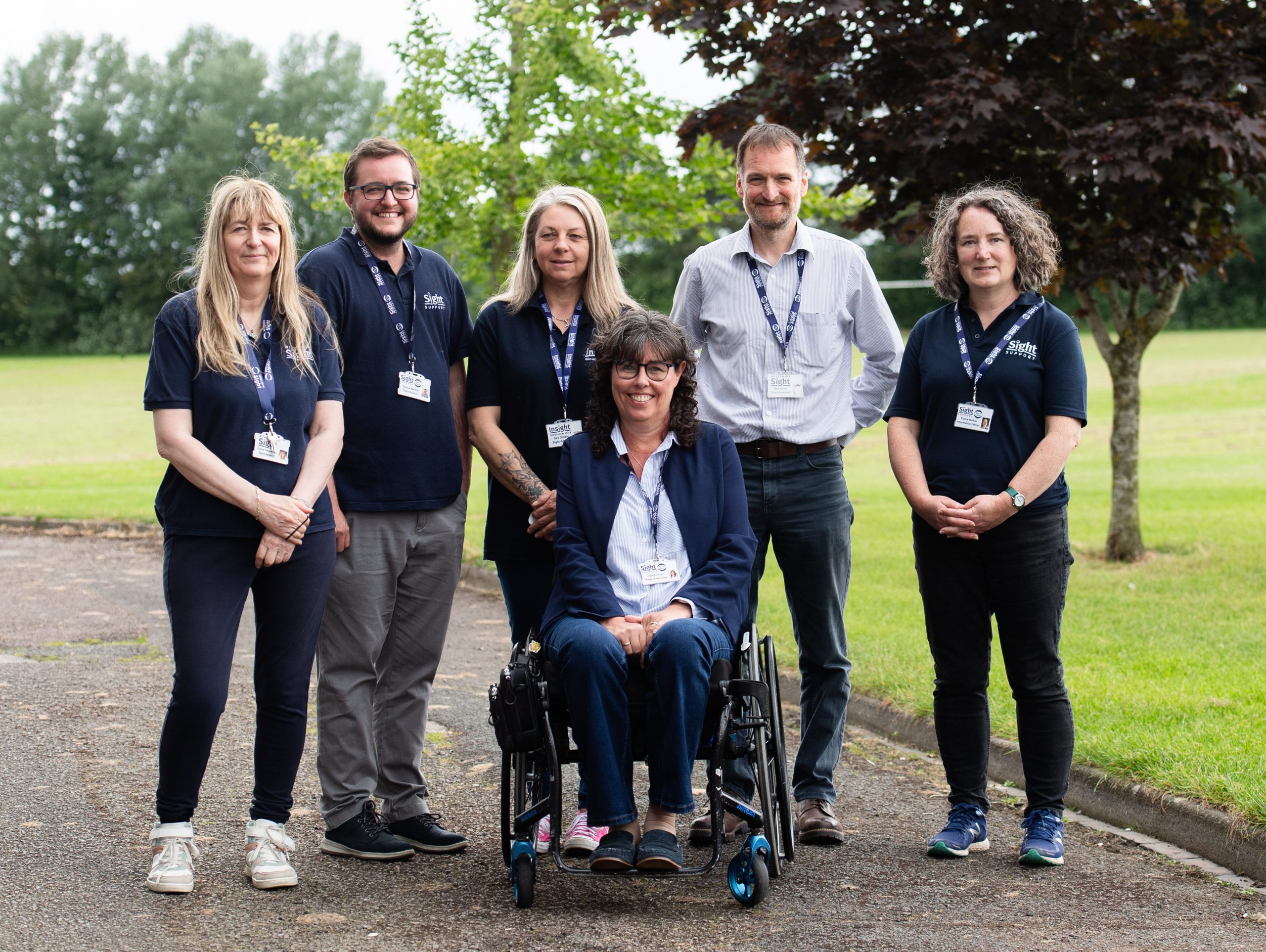 Six members of the Sight Support West of England team outdoors with grass and trees in the background.