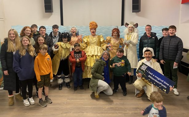 Cast of Dick Whittington Aberdeen Arts Centre in full costume with children and young people and NESS team. Dick Whittington is kneeling and holding a sign that says "I had a magical time at #AberdeenPanto." and has "Aberdeen Arts Centre" on the left hand of the sign. Photo by NESS.