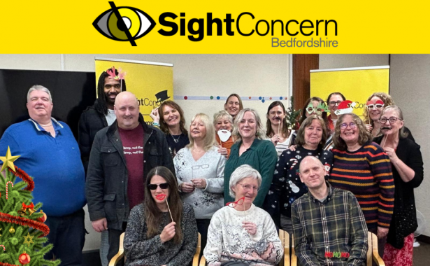 Sight Concern Bedfordshire team and service users holding sticks with glasses, santa beard, santa hats and the words "ho, ho, ho," There is a decorated christmas tree on the left hand side. The Sight Concern Bedfordshire logo is at the top.