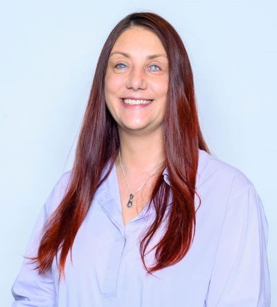 Nina smiling with her long red hair open and wearing a lilac blouse and silver pendant.