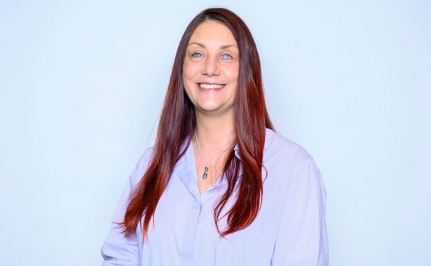 Nina smiling with her long red hair open and wearing a lilac blouse and silver pendant.