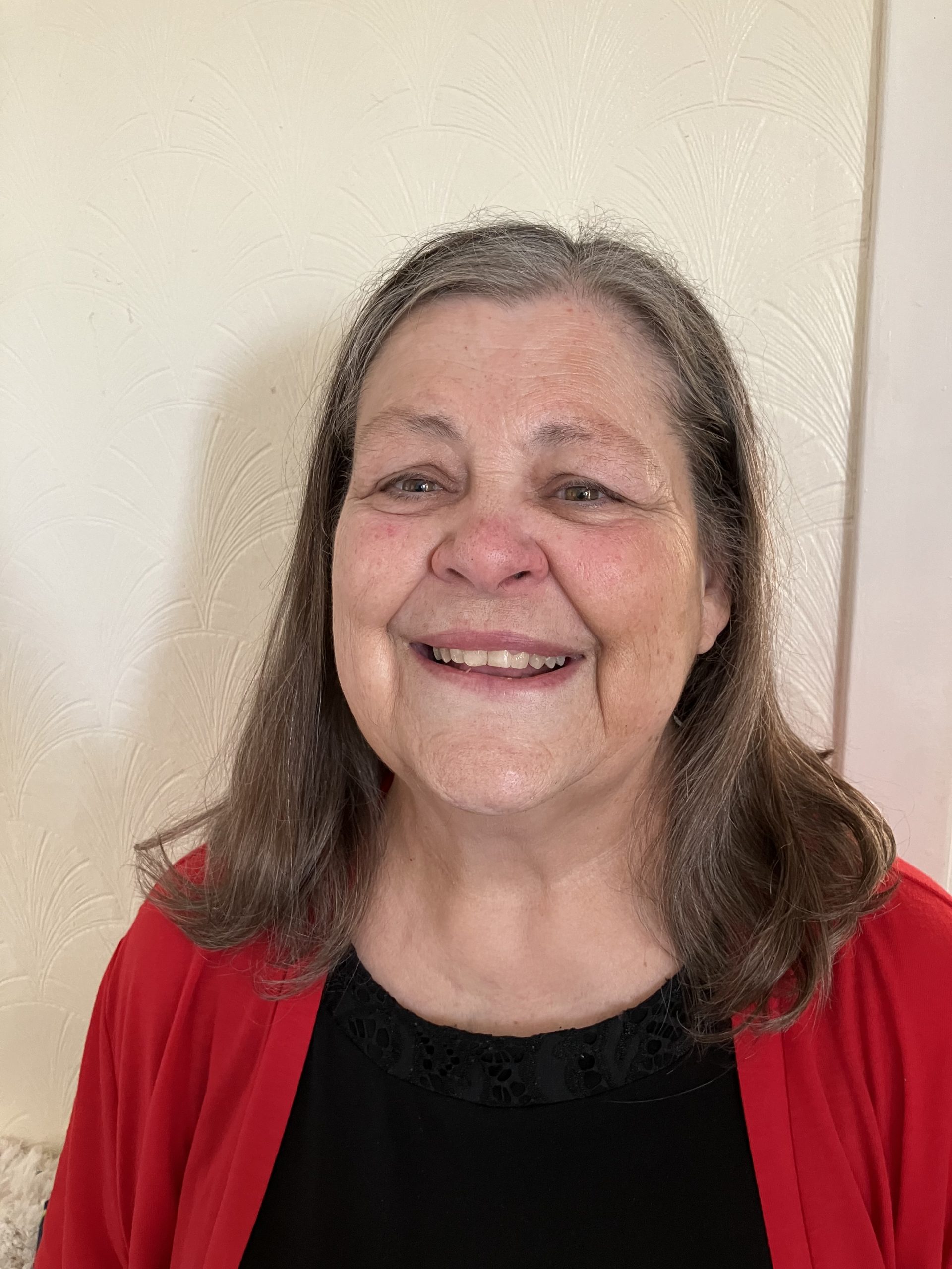 Jan Harrision smiling, with shoulder length hair, wearing a black top and red cardigan.